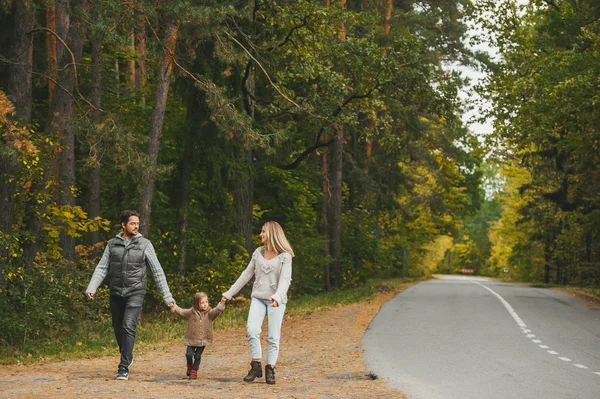 Happy family of three, holding hands, walk on a country asphalte road road in autumn day — Stock Photo, Image
