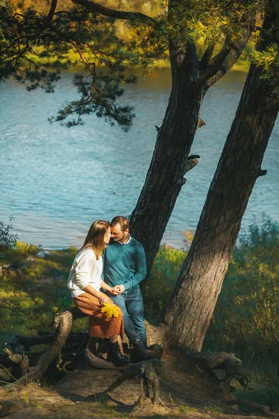 Hermosa pareja romántica sentada bajo el árbol en la orilla del río y besándose en el día de otoño — Foto de Stock