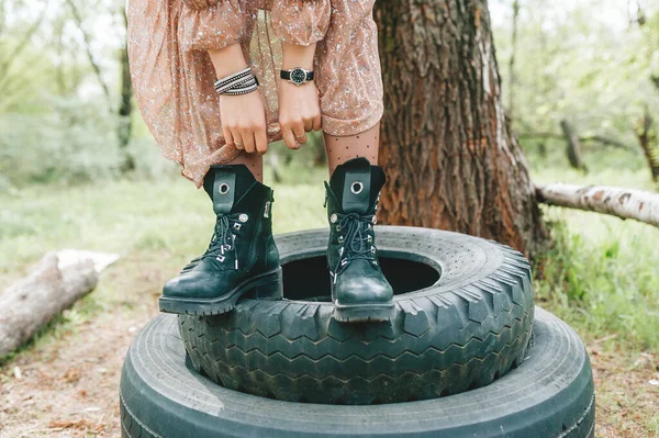 穿着黑色皮靴站在自然轮胎上的女孩的腿 闭包视图 — 图库照片