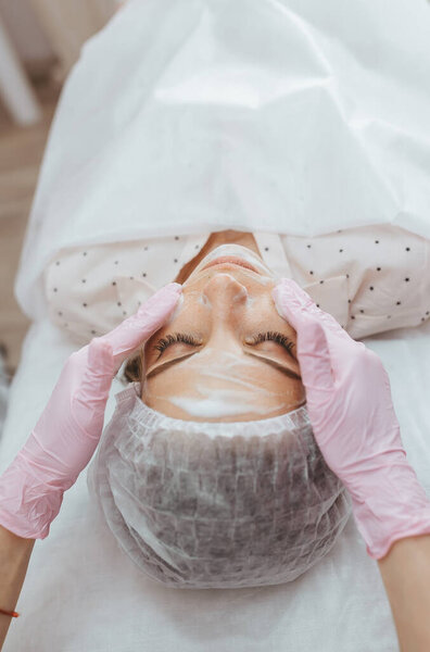 Beautician cleans alginate mask from the face of her patient. Top view.