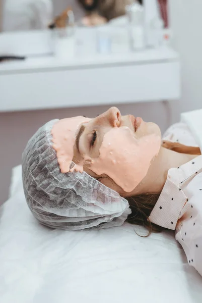 Cosmetologist is applying mask on woman client face in beauty clinic. Portrait of woman, side view. Beautician making beauty facial skincare procedure to patient. Beauty industry concept.