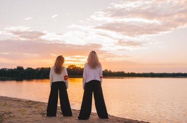 Güneş doğarken yoga meditasyonu yapan iki kadın. Sahilde ya da nehir kıyısında sabah yogası. Arka plan. 