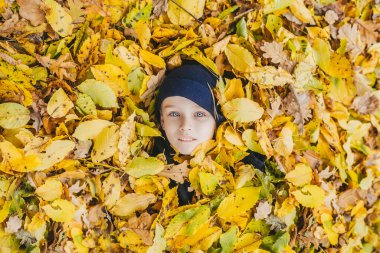 Büyük bir yaprak yığınının üzerinde yatarken gülümseyen mutlu çocuk. Üst görünüm