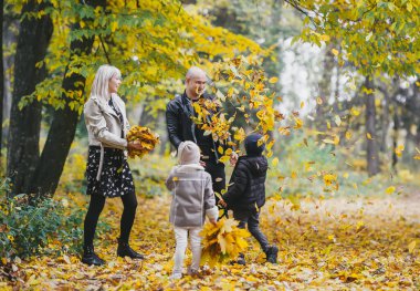 Beyaz bir aile sonbaharda yapraklarla dolu bir parkta eğleniyor. Parlak sarı ağaçlar ve yapraklar.