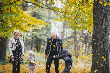 Sonbahar parkında mutlu bir aile fotoğrafı, güz ormanlarında oynayan neşeli bebekleri olan ebeveynler, kızlarıyla ve oğluyla sonbahar ormanlarında eğlenen anne ve baba. Mutluluk konsepti, zevk zamanı.