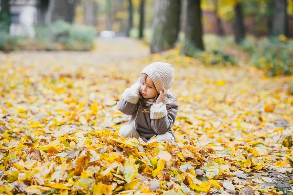 在一个美丽的秋日 穿着保暖衣服的小女孩在干枯的树叶中玩乐 — 图库照片
