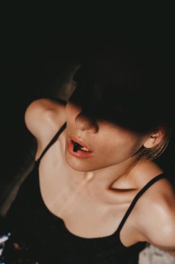 Yüzünde gölgesi olan genç bir bayanın sürrealist sanat portresi. Sıra dışı kirpikleri olan çekici bir genç kadın ağzında hap kapsülü tutuyor. Güzellik, moda ve tıp. Stüdyo çekimi.