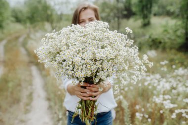 Kırsalda bir buket kır çiçeğini kucaklayan güzel kız. Çiçeklerde seçici odak