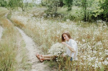 Orman yolunda beyaz kır çiçekleriyle oturan mutlu kadın. Yatay portre