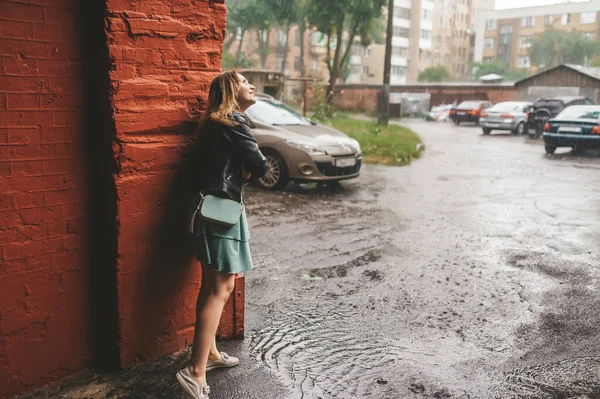 美丽的微笑的女孩正在城市的庭院里等待着雨的结束 仰望着天空 — 图库照片