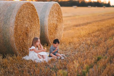 Sevimli küçük çocuklar saman yığınının ya da balyanın yanında oturup hayal kuruyorlar. Sıcak yaz akşamlarında gün batımında açık hava eğlencesi..