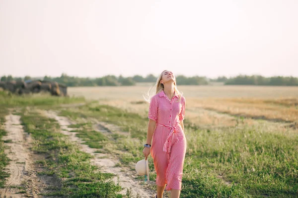 Szczęśliwa Blondynka Czerwonej Sukience Idzie Samotną Drogą Przez Pole Widok — Zdjęcie stockowe