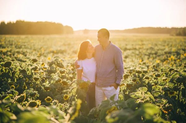 夕暮れ時にひまわり畑で抱き合う幸せなカップル 白い夏のブラウスの女の子 ジーンズの男とシャツ 夏休みのコンセプト — ストック写真