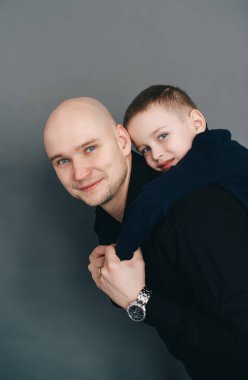 Neşeli kel baba ve siyah elbiseli oğlu stüdyoda koyu bir geçmişi olan poz veriyorlar. Aile fotoğrafı.