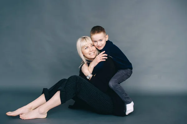 喜びの家族は黒い服の彼女の息子が暗い背景と床にポーズをとっているブランド 肖像画 — ストック写真