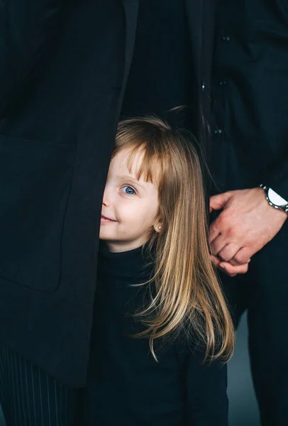 Uma Menina Encantadora Escondida Atrás Das Roupas Pretas Dos Pais — Fotografia de Stock