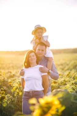 Baba, anne ve kız hasır şapkalı gün batımında ayçiçeği tarlasında. Aile yaz tatili seyahati. Köyde tatiller. Özgürlük kavramı.
