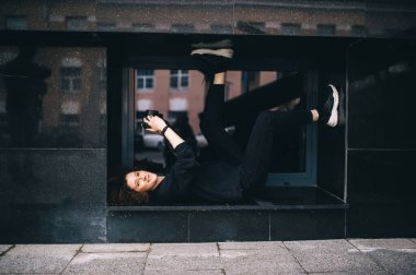 Elinde kamera olan bir kadın, şehir caddesinde mermer bir binanın penceresinde arkasında yatıyor. Kadın fotoğrafçı.