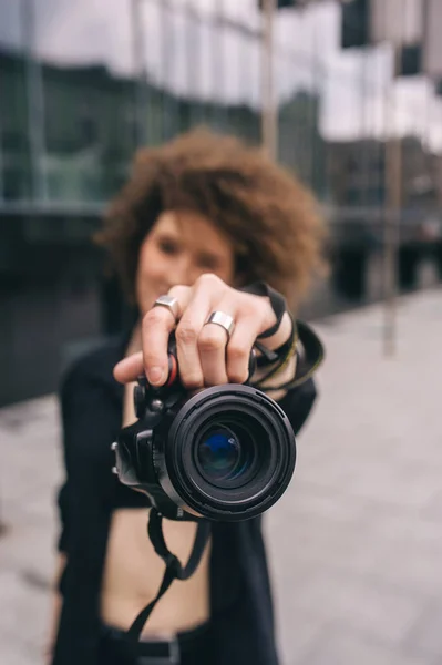 摄影记者用数字50毫米镜头反射式相机拍照 年轻的卷曲女孩用镜像相机给你拍照 城市街道上拿着镜头的摄影师 专注于镜头 — 图库照片