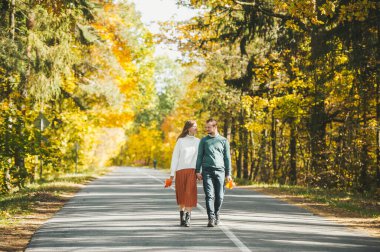 Birbirlerine aşık genç ve şık bir çift sonbahar tarzı yolda yürüyor ve birlikte mutluluğu hissediyorlar. Yatay portre