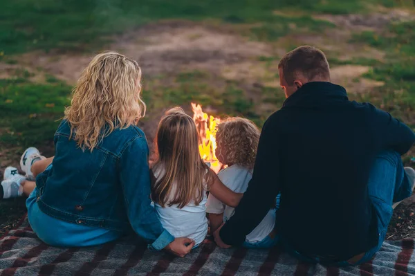 stock image Happy family of four are sitting on a grass by the fire and watching the sunset. Back view  