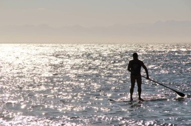 Denizdeki bir sörfçünün güneş ışığındaki siluetin görüntüsü