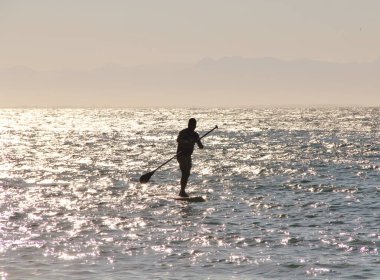 Denizdeki bir sörfçünün güneş ışığındaki siluetin görüntüsü