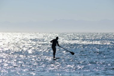Denizdeki bir sörfçünün güneş ışığındaki siluetin görüntüsü