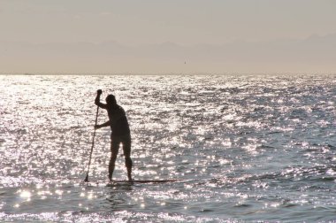 Denizdeki bir sörfçünün güneş ışığındaki siluetin görüntüsü