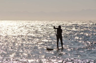 Denizdeki bir sörfçünün güneş ışığındaki siluetin görüntüsü