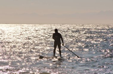 Denizdeki bir sörfçünün güneş ışığındaki siluetin görüntüsü