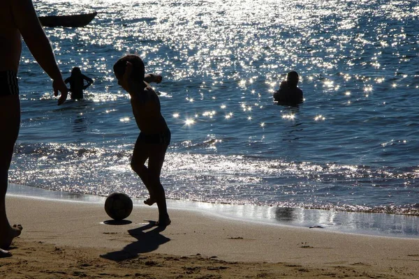 Futbol oynayan, yüzen ve kumsalda dinlenen insanları izleyin. 