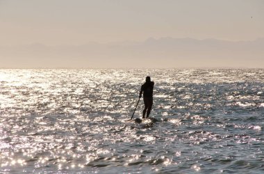 Denizdeki bir sörfçünün güneş ışığındaki siluetin görüntüsü