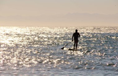 Denizdeki bir sörfçünün güneş ışığındaki siluetin görüntüsü