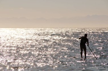 Denizdeki bir sörfçünün güneş ışığındaki siluetin görüntüsü