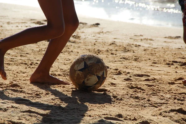 Garoto Joga Bola De Futebol Na Praia Arenosa. Pés Descalços De