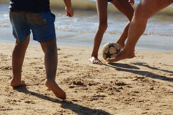 Garoto Joga Bola De Futebol Na Praia Arenosa. Pés Descalços De