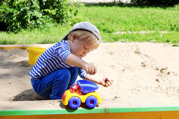 Child playing in the sandbox with toy car