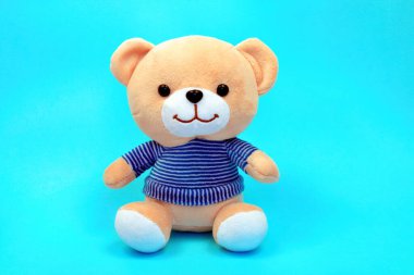 Mavi arka planda izole edilmiş çizgili süveterli oyuncak ayı.