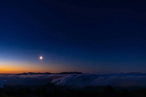 Early morning on mountains with moon over a  sea