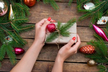 Ladin filizinden yapılmış el işi kağıdına sarılı bir hediye. Noel ağacı süslemeleri ve bir Noel ağacının dalları. Eller hediyeyi çözsün. Koyu renk ahşap kaplama. Düz lei.