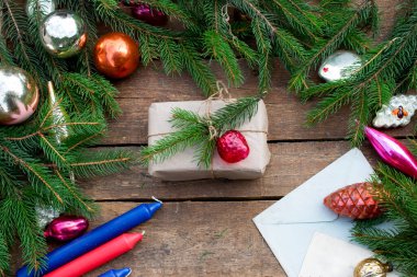 Noel ağacı süslemeleri, köknar ağacı dalları, kırmızı başlık, mumlar. Ladin filizinden yapılmış el işi kağıdına sarılı bir hediye. Koyu renk ahşap kaplama. Düz lei.