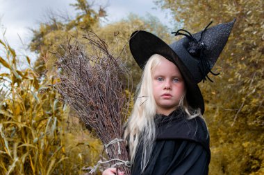 Cadılar Bayramı ve cadılar. Sonbahar ormanında elinde süpürgeyle siyah şapkalı bir kız.