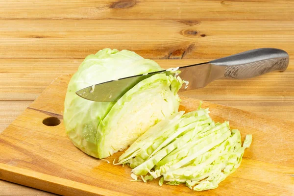 Sliced cabbage, knife on cutting board, half cabbage head. Fresh vegan food. Sliced cabbage on a cutting board. Wooden background