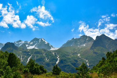 Kafkas Dağları 'nın karla kaplı zirvelerinin güzel bir manzarası. Mavi gökyüzüne karşı beyaz bulutlar.