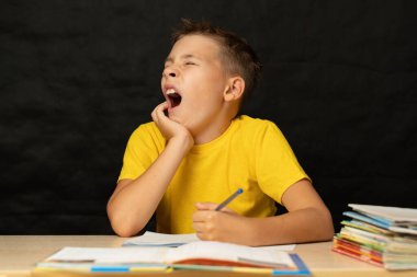 Çocuk esniyor, masasında oturuyor ve ödev yapıyor. Çocuk sıkıcı derslerden esniyor..