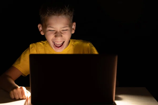 Bir çocuk yüksek sesle gülüyor, karanlıkta bir video izliyor, dizüstü bilgisayar ekranında.