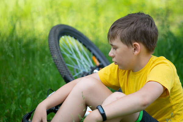 После падения с велосипеда ребенок садится на траву
.