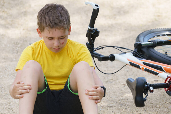 избитый ребенок, сидящий на земле с опущенной головой
