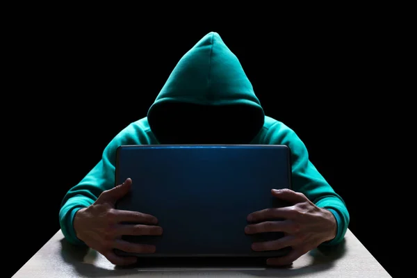 Unknown person in the hood, reaches out from the darkness to the laptop. Theft of household and computer equipment.